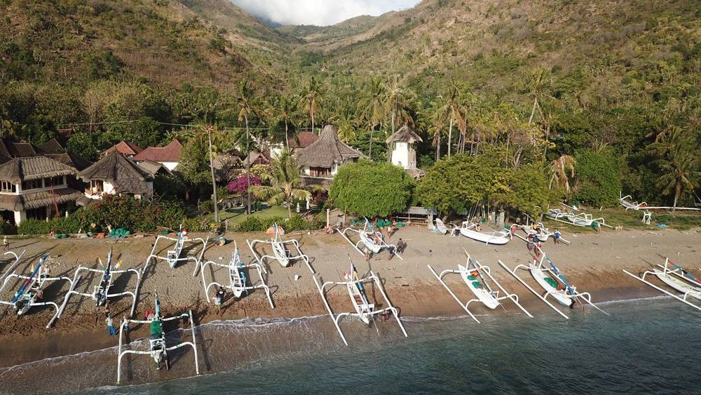 Aerial view of Life in Amed on the beach in Lean village, with jukung boats and green hills behind