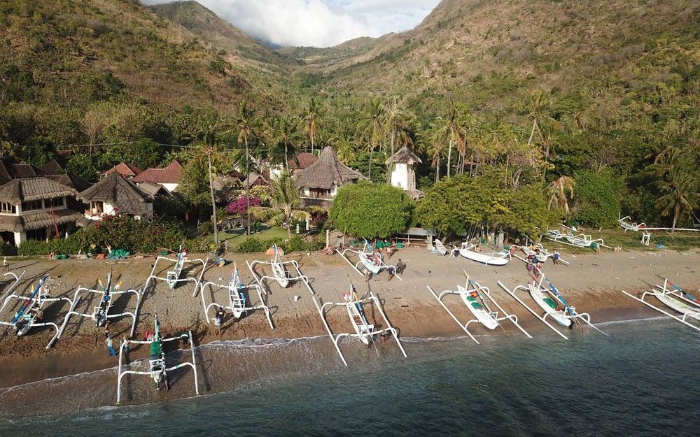 Aerial view of Life in Amed on the beach in Lean village, with jukung boats and green hills behind