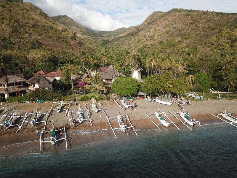 Aerial view of Life in Amed on the beach in Lean village, with jukung boats and green hills behind