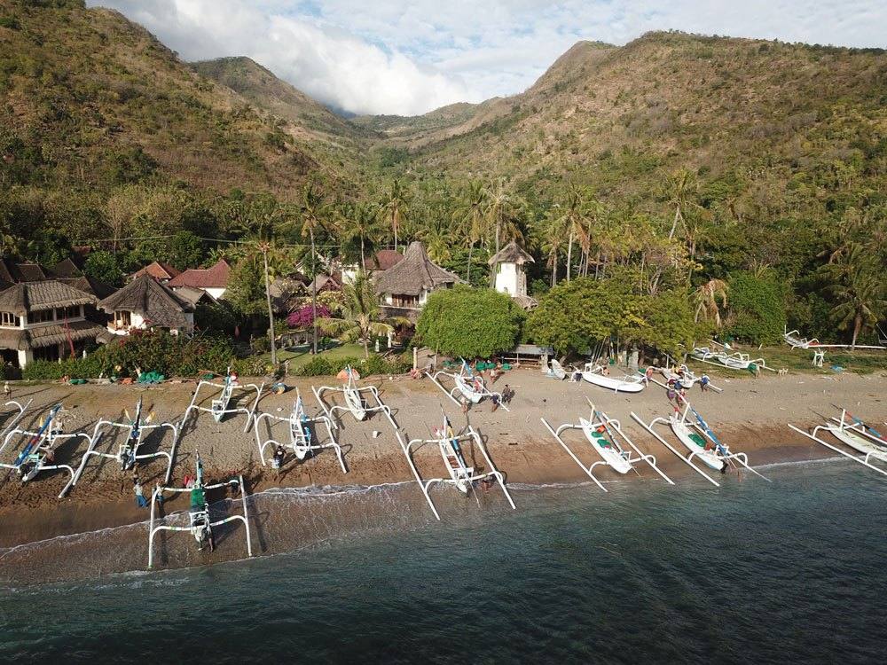 Aerial view of Life in Amed on the beach in Lean village, with jukung boats and green hills behind