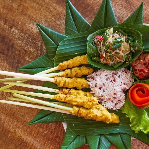 Balinese sate lilit on lemongrass sticks with rice and sambal on a banana leaf