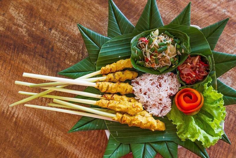 Balinese sate lilit on lemongrass sticks with rice and sambal on a banana leaf