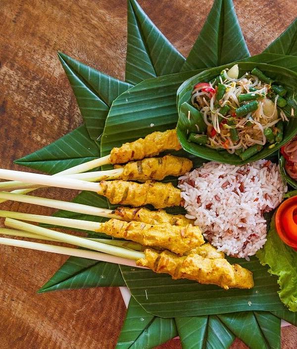 Balinese sate lilit on lemongrass sticks with rice and sambal on a banana leaf