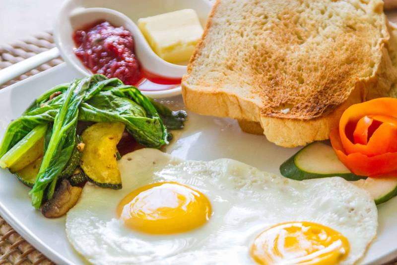 Breakfast of fried eggs, toast, sautéed greens and jam