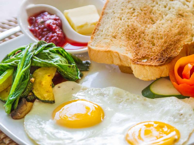 Breakfast of fried eggs, toast, sautéed greens and jam