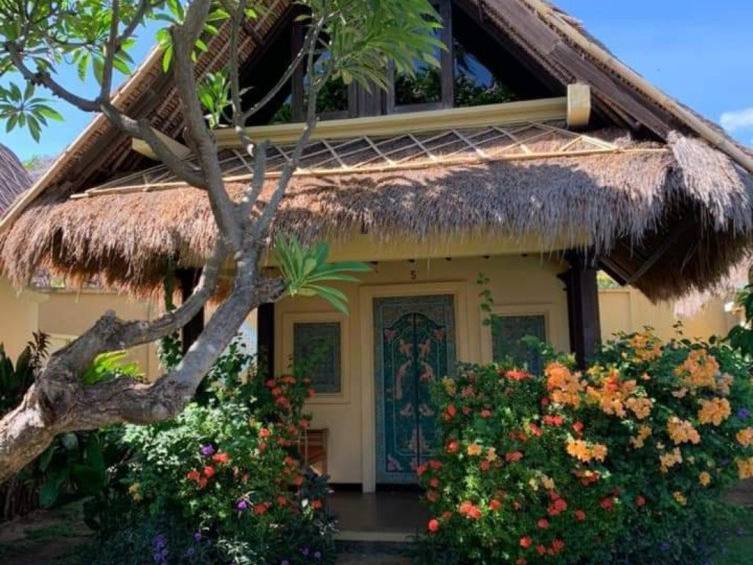 A thatched Beach Cottage among orange flowers and a frangipani tree