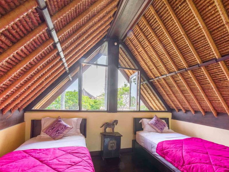 Two single beds in the thatched-roof loft of a Beach Cottage