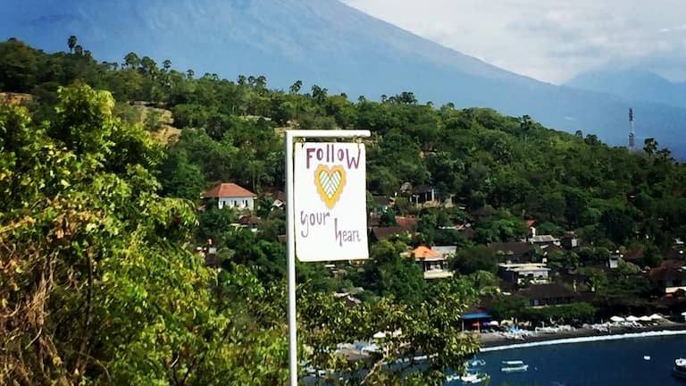 The heart-shaped Life in Amed sign with Mount Agung and the Amed coast behind