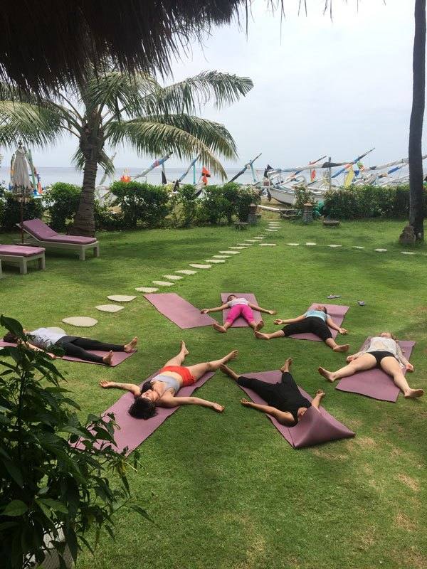 Yoga students resting in savasana on the lawn under the palms