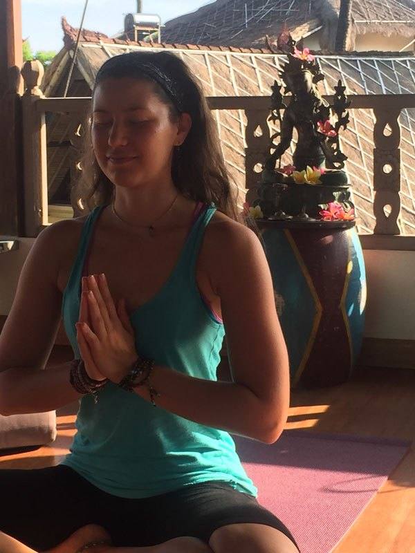 A woman meditating with hands in prayer position in the shala