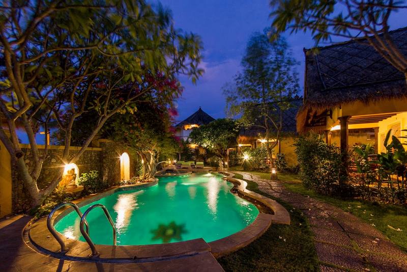 The lit swimming pool and thatched cottages at night