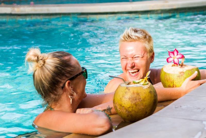 Two guests laughing in the pool with fresh coconuts