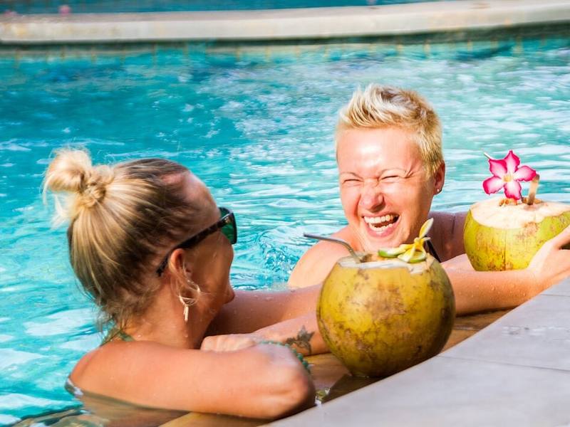 Two guests laughing in the pool with fresh coconuts