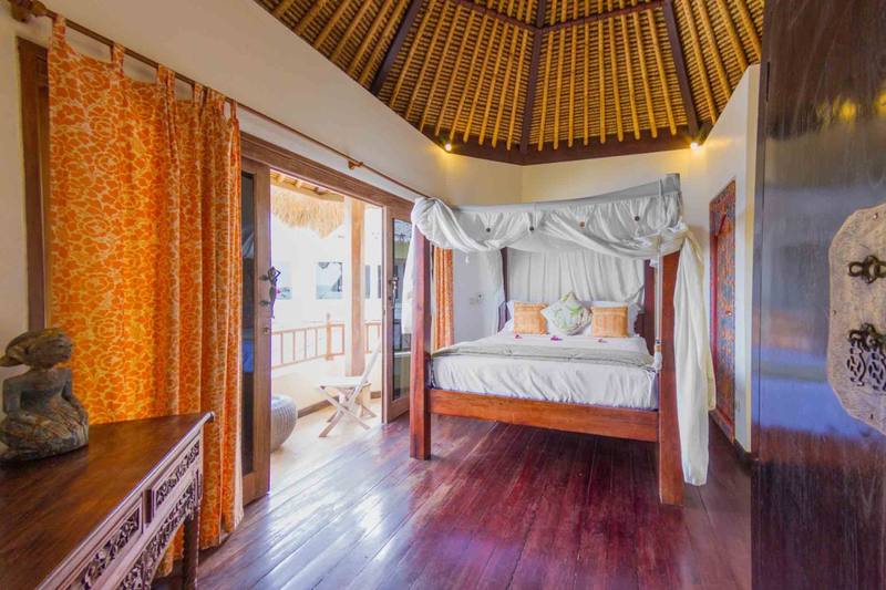 Canopy bed and orange curtains in Sari Sunrise Villa, with the sea beyond