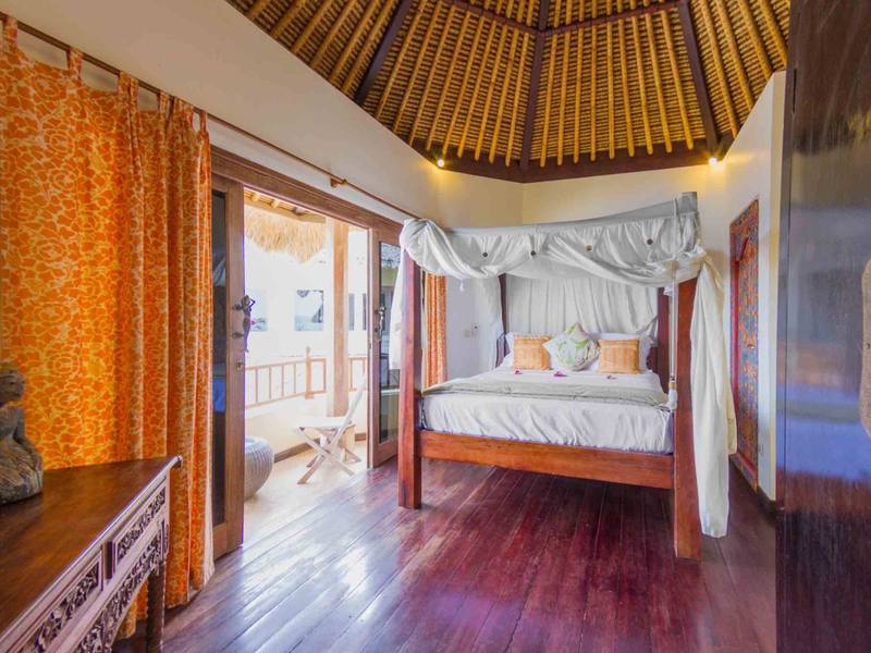 Canopy bed and orange curtains in Sari Sunrise Villa, with the sea beyond