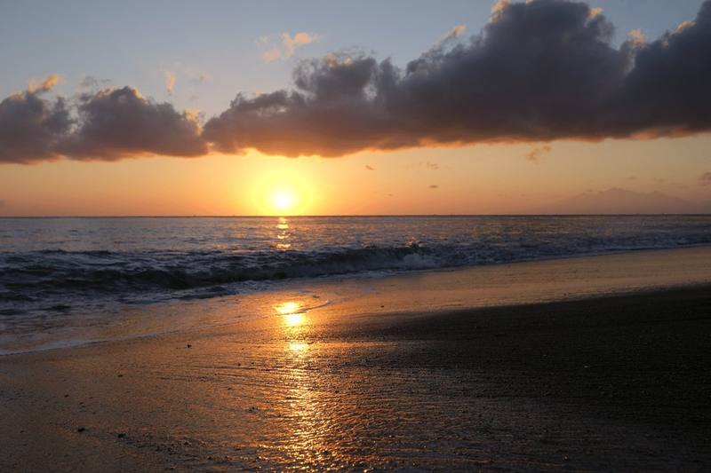 The sun rising over the sea in front of the black-sand beach in Amed, Bali