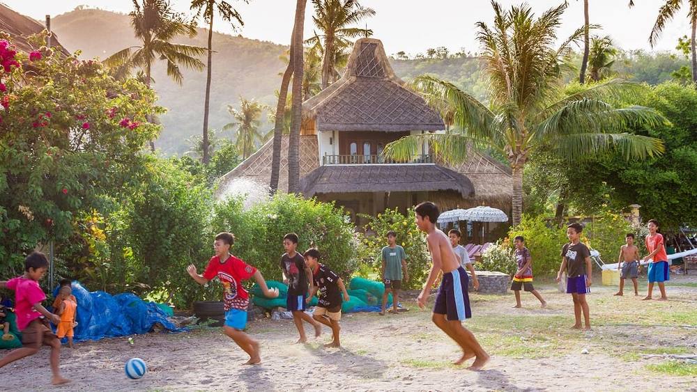 Children from Lean village playing football on the beach in front of the jukung boats