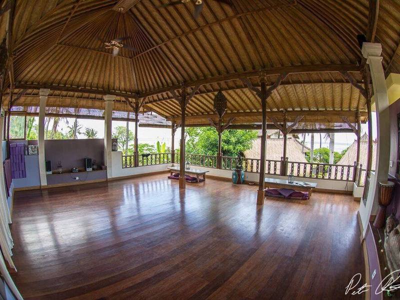 The empty yoga shala with polished wooden floor and thatched roof