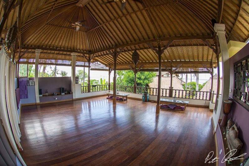 The empty yoga shala with polished wooden floor and thatched roof